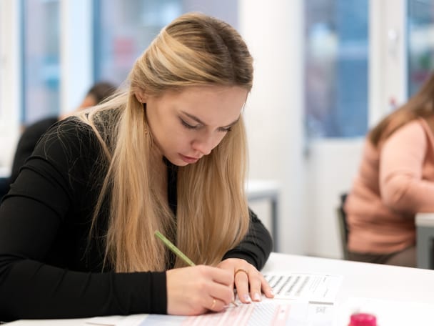 Mensch sitzt am Tisch und schreibt. 