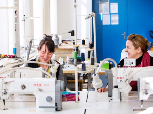 Zwei Menschen sitzen an Nähmaschinen. 