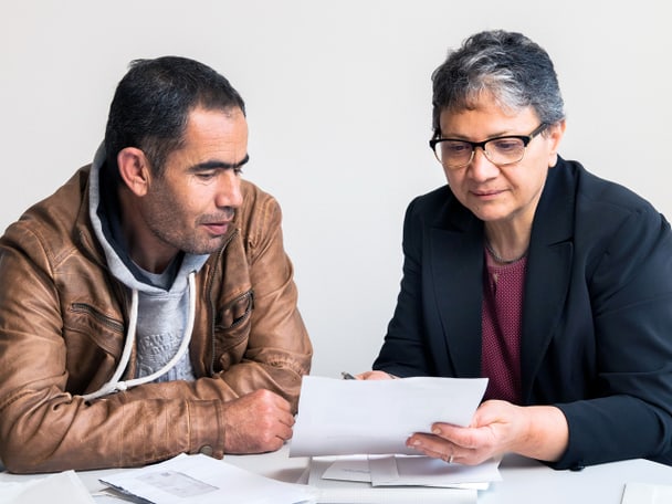 Zwei Menschen sitzen am Tisch und betrachten ein Blatt Papier.