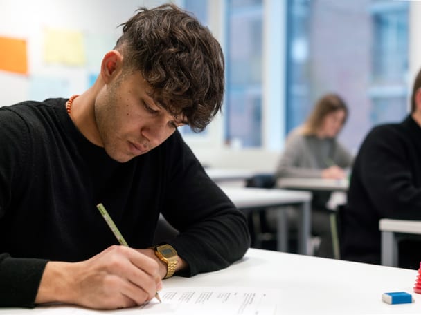 Mensch sitzt am Schreibtisch und schreibt. 