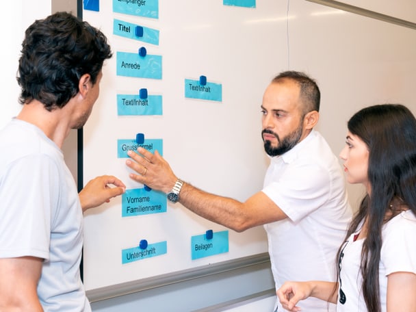 Drei Kursteilnehmende im Gespräch vor einem Whiteboard
