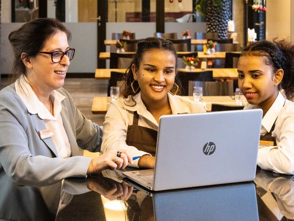 Drei Menschen sitzen vor einem Laptop.