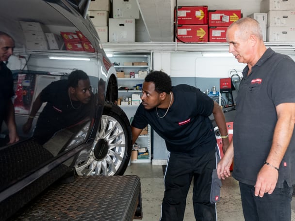 Zwei Männer untersuchen ein Auto in einer Werkstatt.