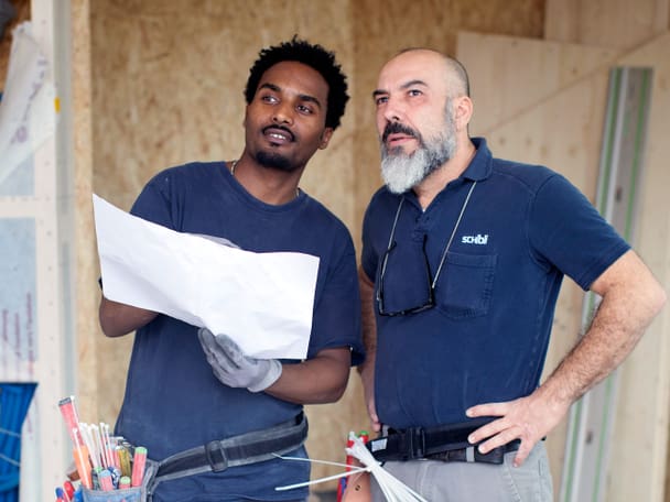 Zwei Männer betrachten einen Plan in einer Baustelle.