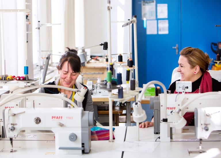 Zwei Menschen sitzen an Nähmaschinen.
