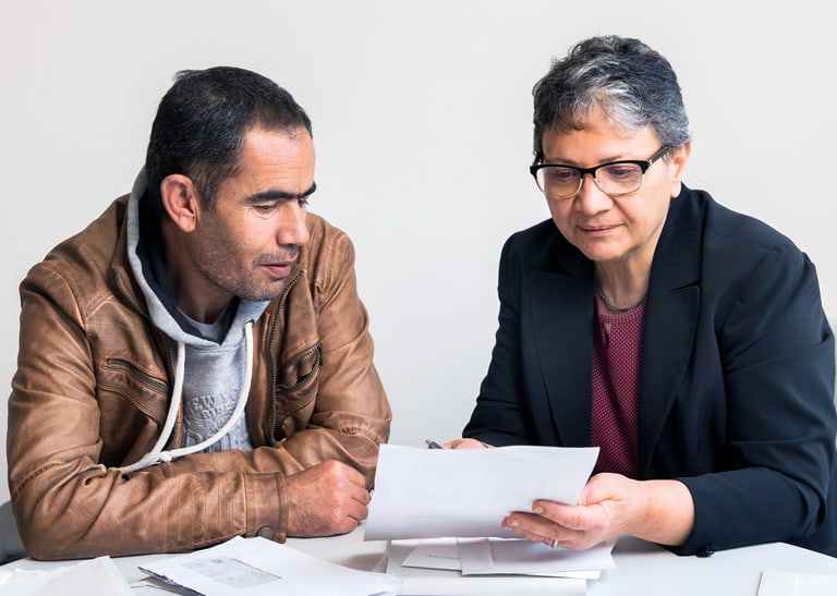 Zwei Menschen sitzen am Tisch und betrachten ein Blatt Papier.