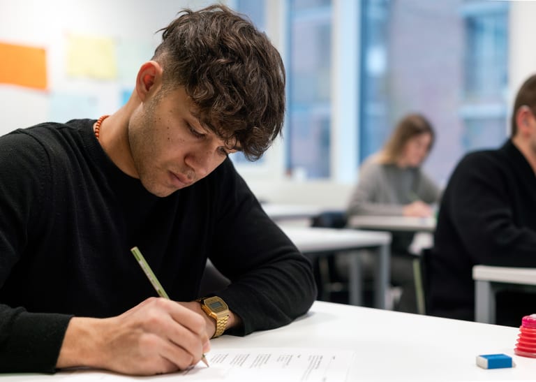 Mensch sitzt am Schreibtisch und schreibt.