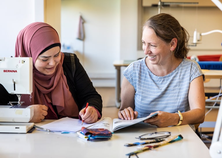 Zwei Menschen sitzen vor einer Nähmaschine.
