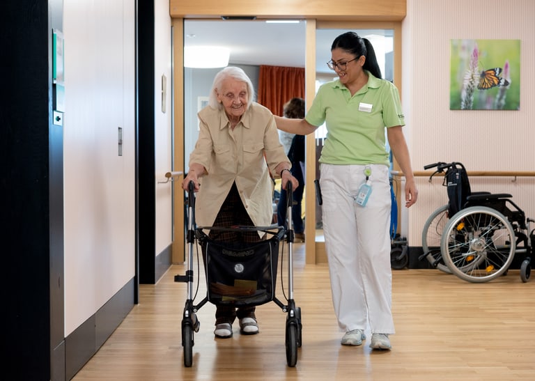 Eine Pflegefachperson begleitet einen älteren Menschen am Rollator.