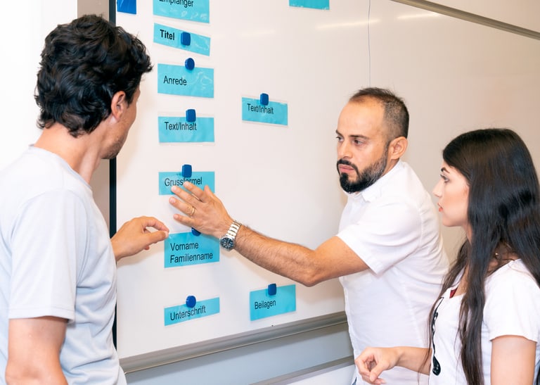 Drei Kursteilnehmende im Gespräch vor einem Whiteboard