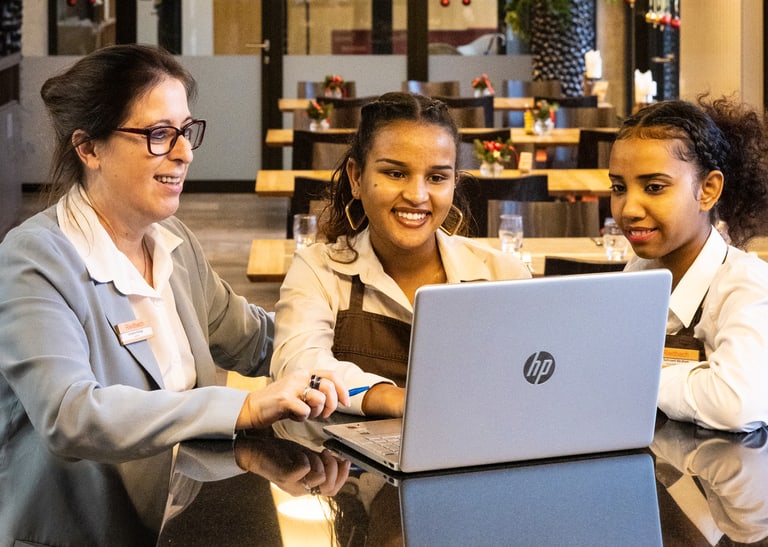 Drei Menschen sitzen vor einem Laptop.