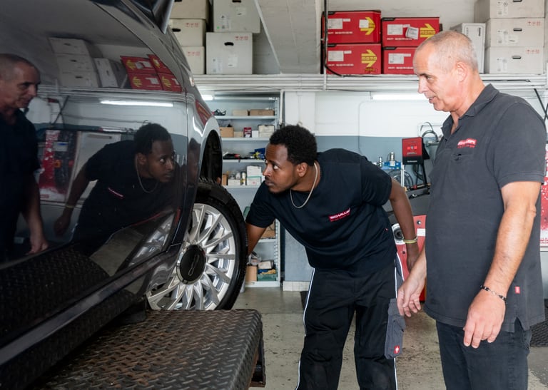 Zwei Männer untersuchen ein Auto in einer Werkstatt.