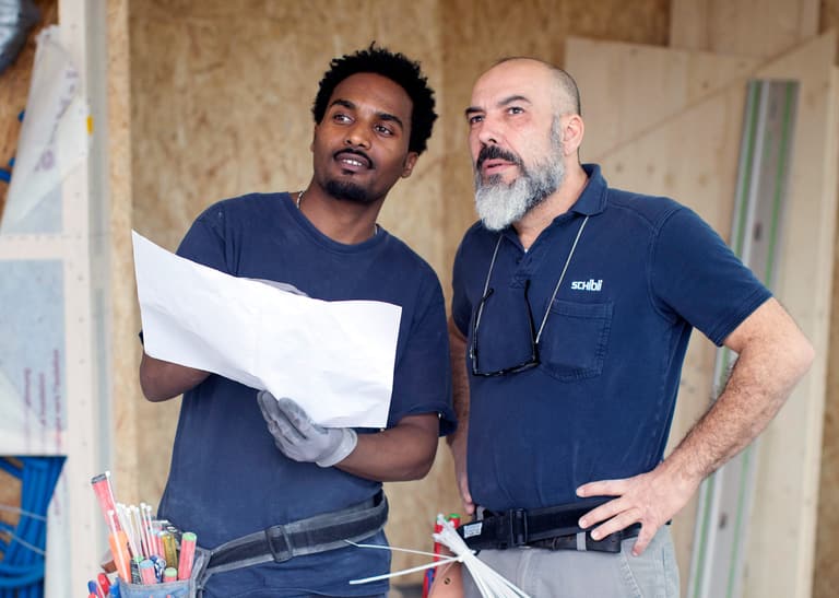 Zwei Männer betrachten einen Plan in einer Baustelle.