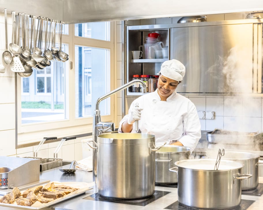 Köchin steht vor einem grossen Kochtopf